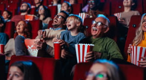 Spotlight on Father, daughter and grandfather laughing whilst watching a movie at the cinema eating popcorn. 